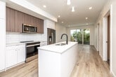 This thoughtfully designed single-floor residence showcases a clean, contemporary aesthetic throughout. The open-concept kitchen is a standout feature, centered around a large white quartz island with an undermount sink and matte black faucet. Cabinetry combines crisp white lower units with warm wood-toned upper cabinets, complemented by a classic subway tile backsplash. Stainless steel appliances, including a French door refrigerator, electric range, and built-in microwave, complete the well-equipped kitchen.

Light wood-toned flooring flows seamlessly throughout the living spaces, enhancing the bright, airy atmosphere created by recessed lighting and large windows. The living area opens to an outdoor balcony through sliding glass doors, offering pleasant tree-lined views.

The bedrooms are generously proportioned and filled with natural light from large windows and sliding doors, each offering views of the surrounding greenery. The primary bathroom features a wide wood-grain vanity with a white quartz countertop and an oversized mirror, paired with neutral tile flooring and a tiled walk-in shower. A separate half bath offers a pedestal sink, toilet, and wood-look flooring for added convenience. The overall ambiance is fresh, minimal, and move-in ready.