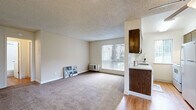 This 1-bedroom, 2-bathroom unit in Carmichael, California offers a practical and well-organized single-floor layout. The open-concept living, dining, and kitchen area forms the heart of the home, with plush carpet in the living and dining zones transitioning to hardwood flooring in the kitchen. A large window in the living area floods the space with natural light and offers views of the surrounding greenery, while a ceiling fan adds comfort to the adjoining area. The kitchen is equipped with dark wood cabinetry, a white refrigerator, an electric range, a single-basin sink, and a light countertop, all illuminated by a skylight window. The bedroom is a comfortable, carpeted retreat featuring a sliding-door closet and direct access to one of the two bathrooms, which includes a vanity with dark wood cabinetry and a mirror. The second bathroom features a full tub-shower combination with hardwood flooring. A textured popcorn ceiling is consistent throughout the unit. Two closets provide ample storage. Neutral wall tones and windows with vertical blinds contribute to a clean, functional ambiance throughout the space.