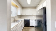 This two-story residence offers a well-organized layout spread across two levels, connected by a staircase visible in the three-dimensional floor plan. The main level features open living areas finished with dark hardwood-style flooring and neutral taupe-toned walls, creating a clean and versatile backdrop. Textured popcorn ceilings are consistent throughout the home, adding a classic finish overhead, while white baseboards provide a crisp contrast along each room.

The kitchen is efficiently designed in a U-shaped configuration, outfitted with white shaker-style cabinetry, light stone-patterned countertops, and a double-basin stainless steel sink positioned beneath a window with blinds. Black appliances, including a refrigerator, dishwasher, and range, complete the functional setup. A dedicated utility area on the main level houses the water heater alongside washer and dryer hookups.

Upstairs, the bedrooms are finished with soft carpeting and neutral walls, offering a comfortable and quiet atmosphere. Natural light filters in through windows fitted with blinds. The bathroom includes a tub-shower combination with clean white surround panels, wood-look tile flooring, and textured walls, providing a practical and tidy space.