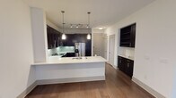 Located at 3509 N Grapevine Mills Blvd in Grapevine, TX, this single-floor unit showcases a contemporary design with a cohesive, open layout. Rich dark hardwood flooring flows throughout the main living areas, lending warmth and contrast against the crisp white walls and ceilings.

The kitchen is a standout feature, equipped with dark espresso cabinetry that extends to the ceiling, sleek white countertops, a subway tile backsplash, and a full suite of stainless steel appliances including a refrigerator with ice maker, range, microwave, and dishwasher. A large center island with pendant lighting provides additional prep space and casual seating. A built-in shelving unit and a dedicated wet bar area with additional cabinetry add both function and character nearby.

The open living area is bright and generously proportioned, benefiting from natural light through French doors that lead to an exterior access point. Track lighting and a ceiling fan complement the space.

The bathroom features a dual-sink vanity with dark cabinetry and a wide mirror, tile flooring, and a combination tub and shower with tile surround. A carpeted bedroom with a ceiling fan and a window with natural light completes the layout, offering a comfortable and quiet retreat.
