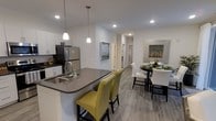 Located at 1555 Ridge Boulevard in Traverse City, Michigan, this single-floor residence offers a thoughtfully designed open-concept layout that seamlessly connects the kitchen and dining areas. The kitchen is a standout feature, showcasing white cabinetry, dark quartz countertops, and stainless steel appliances, including a full-size refrigerator. A large central island with a built-in sink and striking pendant lighting serves as both a functional workspace and a casual dining spot, complemented by vibrant yellow upholstered bar stools that add a pop of color. Recessed lighting throughout ensures the space remains bright and welcoming. The dining area flows naturally from the kitchen, providing an intimate setting for meals and gatherings. Wide-plank wood-look flooring runs throughout the space, adding warmth and cohesion to the overall aesthetic. Crisp white walls create a clean, modern backdrop, while carefully placed artwork adds character and visual interest. The hallway connects to additional areas of the residence, maintaining an efficient and logical floor plan. Overall, the space strikes a balance between modern design sensibility and everyday functionality, making it a comfortable and stylish living environment.
