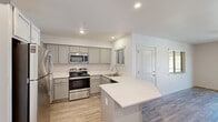 Located at 5555 N Dante Ave in Fresno, CA, this 2-bedroom, 2-bathroom residence offers a thoughtfully designed single-floor layout. The open-concept living, dining, and kitchen area serves as the heart of the home, bathed in natural light and finished with durable wood-style flooring. The kitchen is well-equipped with stainless steel appliances including a refrigerator, range, and microwave, complemented by grey shaker-style cabinetry, a white quartz peninsula with bar seating, and recessed lighting overhead. The living area features a ceiling fan and sliding glass doors that open to a private balcony, offering pleasant outdoor views. Both bedrooms are carpeted and bright, with the primary bedroom featuring its own dedicated closet. Three closets total provide ample storage throughout. Each bathroom is finished consistently with wood-style flooring, grey vanity cabinetry, white quartz countertops, and tub-shower combinations with glass enclosures. A dedicated laundry area and a hallway connecting the main spaces complete the practical and cohesive layout. The clean, neutral palette and modern finishes throughout give the home a fresh, move-in-ready feel.