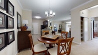 This single-floor residence offers a thoughtfully designed open layout that connects the main living areas seamlessly. The dining area is anchored by a round wood table beneath a brushed nickel chandelier, with crown molding and neutral carpet continuing throughout. Adjacent, the kitchen features dark espresso cabinetry, granite countertops, tile flooring, and black appliances including a full-size refrigerator and dishwasher. A dedicated in-unit laundry area is conveniently accessible nearby.

The living room is a comfortable gathering space highlighted by a tiled fireplace with a built-in media niche above it, crown molding, and plush carpet underfoot. A sliding glass door floods the room with natural light and opens to a private outdoor balcony with views of greenery. The primary bedroom is spacious, offering large windows, soft carpeting, and ample room for a king-size bed. A second bedroom provides similar comfort and natural light. The full bathroom includes a dark vanity with a white countertop, tile flooring, and a tub-shower combination, completing this well-rounded residence.