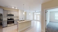 Located on E Buckhill Rd in Burlington, NC, this single-floor residence offers a thoughtfully designed open-concept layout with modern finishes throughout. The kitchen serves as the centerpiece of the main living area, showcasing granite countertops, a large island with an undermount sink, stainless steel appliances including a refrigerator, electric range, and microwave, as well as gray shaker-style cabinetry with a subway tile backsplash. Stylish pendant lighting and a track lighting system illuminate the space, while the island flows seamlessly into the open living area. The living room features light hardwood-style flooring, a ceiling fan, and French doors that invite natural light and provide access to an outdoor area. The bedrooms are carpeted for comfort and each include ceiling fans and windows with natural light. Closet space is well-provided, with at least one bedroom featuring a walk-in closet with built-in shelving. The bathrooms are finished with granite-topped vanities, gray cabinetry with brushed nickel hardware, and light hardwood-style flooring, maintaining a cohesive aesthetic throughout. Clean, neutral wall tones and consistent trim work contribute to a bright, welcoming ambiance across the entire residence.