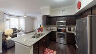 This single-story, 2-bedroom, 2-bathroom residence offers a thoughtfully designed layout that balances functionality with modern style. The kitchen serves as a central highlight, showcasing dark espresso cabinetry, granite countertops, and a full suite of stainless steel appliances, including a range, microwave, dishwasher, and refrigerator. A peninsula with a double undermount sink provides additional prep space and connects the kitchen to the living area, promoting an open flow. A built-in desk nook adjacent to the kitchen offers a convenient workspace. Crown molding throughout adds a refined architectural detail, while dark hardwood-style flooring runs through the main living areas, contrasting cleanly with the neutral wall tones. Both bedrooms are carpeted and receive natural light through windows with blinds and curtain panels. Each bedroom includes a ceiling-mounted light fixture, and the primary bedroom features a walk-in closet. The two bathrooms are finished with granite-topped dark vanities and tile flooring. One bathroom includes a soaking tub and shower combination. The overall ambiance is contemporary and cohesive, with consistent finishes throughout.