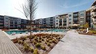 Located at 15621 Bovis Way in Fort Worth, Texas, this outdoor amenity space serves as the central gathering hub of a modern multi-story residential community. The centerpiece is a generously sized, resort-style swimming pool with a graceful curvilinear design and crystal-clear blue water. In-pool loungers allow residents to relax at water's edge, while a shaded pavilion structure with seating provides a covered retreat nearby. Surrounding the pool, a broad concrete sundeck is lined with cushioned wood-frame chaise lounges, ideal for soaking in the Texas sun. Thoughtfully designed landscaping features ornamental grasses, shrubs, and young shade trees throughout, adding texture and greenery to the hardscape. A lush turf lawn area extends across a central courtyard, flanked by concrete walkways and clusters of stylish outdoor seating. String lights overhead enhance the ambiance for evening use. A dedicated sport court is also present, adding a recreational dimension to the space. The entire amenity area is framed by the striking four-story building facades, featuring private balconies, horizontal lap siding, and large windows. Iron fencing creates clear delineation between zones while maintaining an open, connected feel throughout this well-appointed outdoor environment.