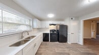 Located at 3450 Evans Rd in Atlanta, GA, this well-appointed single-story home offers three bedrooms, two bathrooms, and a thoughtfully organized layout. The kitchen is a standout feature, showcasing crisp white shaker cabinetry, clean white countertops, a stainless steel sink, subway tile backsplash, and black appliances including a refrigerator, range, and dishwasher — all set above durable wood-look flooring. The open living area flows naturally from the kitchen and is finished with the same wood-look flooring, neutral walls, a ceiling fan, and a sliding glass door that opens to a private balcony with views of surrounding trees. Bedrooms are carpeted for comfort, with the primary bedroom offering generous proportions and ample closet space. Additional bedrooms also feature closets, providing excellent storage throughout. The bathrooms are clean and functional, featuring white tiled tub-shower combinations, vanities with white cabinetry, and wood-look flooring. A dedicated laundry room houses a full-size washer and dryer with built-in shelving above. With four closets distributed across the home and a central hallway connecting all rooms, this residence offers practical, comfortable living in a convenient Atlanta location.