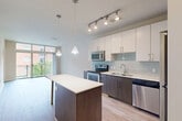 Located at 299 N Highland Ave in Atlanta's dynamic Old Fourth Ward, this modern one-bedroom, one-bathroom residence offers a thoughtfully designed open-concept layout with contemporary finishes throughout. The kitchen is a standout feature, showcasing a two-tone design with crisp white upper cabinetry and dark lower cabinets, a light glass tile backsplash, sleek quartz countertops, and a full suite of stainless steel appliances including a range, microwave, dishwasher, and refrigerator. A center island with pendant lighting provides additional prep space and casual seating. Light wood-style flooring runs through the main living area, complementing the bright, airy atmosphere enhanced by a large sliding glass door that opens to a private balcony with outdoor views. The generously sized bedroom features plush carpeting, a ceiling fan, and ample wall space, offering a comfortable and quiet retreat. The bathroom is finished with large-format white tile flooring, a dark vanity with a white countertop, and a glass-enclosed walk-in shower. Track lighting and pendant fixtures throughout add a modern, polished touch to this well-appointed home.