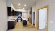 This thoughtfully designed 1-bedroom, 1-bathroom residence is laid out on a single floor, maximizing functionality and comfort. The kitchen serves as the heart of the home, featuring dark espresso cabinetry that contrasts beautifully with light countertops and warm hardwood-style flooring. Stainless steel appliances — including a range, built-in microwave, dishwasher, and a French door refrigerator — provide a sleek, modern aesthetic. A central kitchen island offers additional prep and dining space, making the kitchen both practical and inviting. Recessed lighting illuminates the area with a clean, contemporary feel. Light-toned wood door and window trim throughout adds a warm architectural detail that complements the overall design palette. A dedicated in-unit laundry area is conveniently located just off the kitchen, adding day-to-day practicality. The neutral color scheme of soft whites and warm wood tones creates a bright, welcoming ambiance throughout. The efficient single-floor layout ensures easy flow between spaces, making this residence a smart and stylish option for those seeking modern, low-maintenance living.