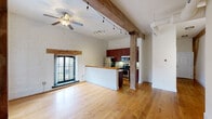 Located at 1329 Jefferson Street in Lynchburg, VA, this one-bedroom, one-bathroom unit masterfully blends historic industrial character with modern finishes. The open-concept kitchen and living area is the heart of the space, defined by striking exposed wood beams, a rustic post column, and whitewashed brick walls that lend an authentic loft aesthetic. Warm hardwood floors run throughout, complementing the natural textures found across every room. The kitchen features rich mahogany-toned cabinetry, stone countertops, a butcher block breakfast bar, and a full suite of stainless steel appliances, including a refrigerator, electric range, and microwave. Arched black-framed windows in the living area invite natural light and frame views of the outdoors, while a ceiling fan with pendant lighting adds both function and charm. The bedroom continues the industrial-chic aesthetic with an exposed wood beam overhead, a double-door closet, and access to the hallway. The full bathroom is clean and functional, equipped with a combination tub and shower. This distinctive space offers a well-considered layout that makes efficient use of its footprint while delivering a unique and characterful living environment.