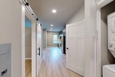 This thoughtfully designed one-bedroom, one-bathroom single-floor unit offers a clean, contemporary aesthetic throughout. Light hardwood flooring runs continuously across all rooms, creating a cohesive and airy feel. The open-concept kitchen and living area serves as the heart of the unit, featuring dark wood cabinetry, white quartz countertops, a black matte sink faucet, and a full suite of stainless steel appliances including a refrigerator, range, microwave, and dishwasher. Recessed lighting illuminates the space efficiently, while a window in the kitchen allows natural light to filter in. A stylish sliding barn door with black hardware adds a modern-industrial design element to the hallway, which connects the main living area to the private rooms. The bedroom is a cozy, well-proportioned retreat finished in neutral tones, equipped with a wall-mounted mini-split HVAC unit and a sliding glass door that opens directly onto a private balcony with outdoor views. The bathroom is neatly appointed with a backlit vanity mirror, wood-toned cabinetry, white quartz countertop, a full tub-shower combination, and black accent hardware throughout. The overall ambiance is clean, modern, and move-in ready.