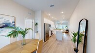 Located at 12556 US-301 in Oxford, Florida, this single-story home offers three bedrooms, two bathrooms, and a thoughtfully designed layout across a comfortable footprint. The interior presents a clean, contemporary aesthetic throughout, characterized by light-toned walls, light wood-look flooring, and an abundance of natural light.

The combined kitchen and living area serves as the heart of the home. The kitchen is outfitted with white shaker-style cabinetry, granite-speckled countertops, a white subway tile backsplash, stainless steel appliances including a refrigerator, range, and built-in microwave, and a central island providing additional prep and dining space. Adjacent to the kitchen, the dining area accommodates a small table and benefits from a window overlooking the front entry. The living room is bright and open, with a ceiling fan and sliding glass doors that allow natural light and outdoor access.

Each of the three bedrooms features ceiling fans, windows with exterior views, and light flooring. The primary bedroom includes a dedicated walk-in closet fitted with wire shelving. Both bathrooms feature white vanities with granite countertops and modern fixtures. A dedicated laundry room houses side-by-side top-load washer and dryer units with overhead wire shelving.