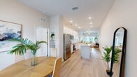 Located at 12556 US-301 in Oxford, Florida, this single-story home offers three bedrooms, two bathrooms, and a thoughtfully designed layout across a comfortable footprint. The interior presents a clean, contemporary aesthetic throughout, characterized by light-toned walls, light wood-look flooring, and an abundance of natural light.

The combined kitchen and living area serves as the heart of the home. The kitchen is outfitted with white shaker-style cabinetry, granite-speckled countertops, a white subway tile backsplash, stainless steel appliances including a refrigerator, range, and built-in microwave, and a central island providing additional prep and dining space. Adjacent to the kitchen, the dining area accommodates a small table and benefits from a window overlooking the front entry. The living room is bright and open, with a ceiling fan and sliding glass doors that allow natural light and outdoor access.

Each of the three bedrooms features ceiling fans, windows with exterior views, and light flooring. The primary bedroom includes a dedicated walk-in closet fitted with wire shelving. Both bathrooms feature white vanities with granite countertops and modern fixtures. A dedicated laundry room houses side-by-side top-load washer and dryer units with overhead wire shelving.