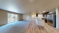 Located at 13105 21st Dr SE in Everett, WA, this single-floor unit offers six bedrooms, two bathrooms, and a thoughtfully designed open-concept layout. The combined kitchen and living area serves as the heart of the home, featuring light hardwood-style flooring, recessed lighting, and a seamless flow between spaces. The kitchen is well-appointed with dark espresso cabinetry, stainless steel appliances including a refrigerator, range, and microwave, along with a light stone countertop and a peninsula with a sink that opens toward the living area. The expansive living room is carpeted and filled with natural light, with sliding glass doors providing direct access to a private balcony overlooking lush, mature greenery. Each of the six bedrooms is carpeted and offers a calm, neutral palette, with select rooms featuring large windows that frame views of the surrounding trees. The primary bedroom includes walk-in closet space with wire shelving for ample storage. The two bathrooms are finished with herringbone-patterned tile flooring, dark wood vanities with dual sinks, wide mirrors, and clean modern fixtures. A hallway connects the private quarters, completing this functional and comfortable layout.