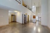 Located at 611 O'Keefe Ave in New Orleans, this two-story, 2-bedroom, 1-bathroom home offers a striking contemporary design that makes a strong architectural statement. The main level is the heart of the home, where soaring double-height ceilings create an impressive sense of volume and openness. Polished concrete floors extend throughout, lending an industrial-modern aesthetic that pairs seamlessly with the clean-lined finishes throughout.

The kitchen is a standout feature, outfitted with light wood cabinetry extending to ceiling height, stainless steel appliances including a range, microwave, dishwasher, and refrigerator, a tiled backsplash, and a white-topped island that adds prep space and casual seating. Pendant lighting drops dramatically from the high ceiling above, reinforcing the loft-like character of the main living area, which is bathed in natural light from large upper windows.

A stacked washer and dryer unit is conveniently tucked within an enclosed closet on the main floor. The bathroom features classic white subway tile surrounding a full tub-shower combination with polished concrete flooring continuing the design language.

Upstairs, the two carpeted bedrooms offer a softer, quieter retreat. The spacious primary bedroom includes a ceiling fan and a built-in closet with sliding mirrored doors and shelving. The second bedroom features track lighting and natural light from a window with views of surrounding greenery.