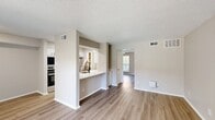 This 580-square-foot, single-story unit at 15678 Knoll Trail Dr in Dallas, TX offers a practical and well-appointed layout comprising a combined kitchen and living area, one bedroom, one bathroom, and a closet. Light wood-style flooring runs throughout the unit, providing a cohesive and clean aesthetic. Neutral warm-beige walls and white trim complement the overall design.

The open kitchen features white shaker-style cabinetry with black hardware, white countertops, a herringbone tile backsplash, stainless steel appliances including a refrigerator and range, and a peninsula with an undermount sink and matte black faucet—offering direct sightlines into the living area.

The living room is spacious relative to the unit's footprint, with a textured ceiling, ceiling fan, HVAC vents, and a sliding glass door fitted with vertical blinds that allows natural light and outdoor views.

The 180-square-foot primary bedroom includes a ceiling fan with light fixture, wood-style flooring, and a window with outdoor views. The bathroom provides a full tub-shower combination with white tile surround, chrome fixtures, a toilet, and a vanity with sink.