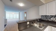 Located at 2545 NE Coachman Rd in Clearwater, Florida, this single-floor unit offers a functional and comfortable layout designed for everyday living. The open-concept living area features soft carpeting and flows seamlessly into the kitchen, which is separated by a peninsula-style breakfast bar with dark granite-look countertops. The kitchen is well-appointed with white cabinetry, a striking black-and-white mosaic tile backsplash, hardwood-style flooring, a double stainless steel sink, and a white electric range with oven. A textured ceiling and recessed lighting complete the kitchen's clean aesthetic. The living room is bright and welcoming, with natural light filtering through multiple windows fitted with horizontal blinds and a ceiling fan overhead. Bedrooms are carpeted and generously sized, with large windows that frame views of surrounding greenery. One bedroom features an expansive wall of windows, while another includes a built-in closet with shelving. Both bathrooms are finished with white vanities, light countertops, full tub-and-shower combinations, and wood-style flooring, offering a clean and practical design. Throughout the unit, neutral tones and consistent finishes create a cohesive and inviting atmosphere.