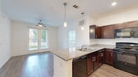 This well-appointed 2-bedroom, 2-bathroom single-floor residence at 1465 Gears Rd in Houston, TX offers a thoughtfully designed layout with a clean, neutral aesthetic throughout. The open-concept kitchen is a standout feature, showcasing rich dark wood cabinetry, granite countertops, pendant lighting over a breakfast bar peninsula, recessed lighting, and black appliances including a refrigerator, range, and microwave. Wood-look plank flooring extends through the main living and kitchen areas, lending warmth and continuity to the space.

Both bedrooms are generously proportioned, carpeted for comfort, and equipped with ceiling fans. Large windows dressed with blinds invite abundant natural light and offer views of the surrounding greenery. The primary bedroom benefits from an en-suite bathroom featuring a granite-topped vanity with dark wood cabinetry, wood-look flooring, and access to a spacious walk-in closet with wire shelving. The second bathroom includes a full tub-shower combo with white tile surround and safety grab bars. A dedicated walk-in closet with carpet flooring and wire rack shelving provides ample storage. The overall ambiance is bright, clean, and move-in ready.