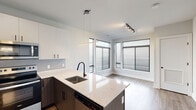 Located at 9 Presidential Blvd in Bala Cynwyd, PA, this thoughtfully designed one-bedroom, two-bathroom residence offers a modern aesthetic with high-quality finishes throughout its efficiently arranged single floor. The open-concept kitchen serves as the centerpiece of the living area, featuring two-toned cabinetry with white upper cabinets and dark lower units, a quartz peninsula countertop, a matte black gooseneck faucet, and a full suite of stainless steel appliances including a refrigerator, electric range, microwave, and dishwasher. A sleek linear pendant light illuminates the peninsula, while a tiled backsplash adds a refined touch. The adjacent dining area benefits from an expansive corner window arrangement that floods the space with natural light. The bedroom is comfortably proportioned, finished with plush carpeting, and features multiple windows fitted with horizontal blinds. A hallway connects the bedroom to the two bathrooms, one of which includes a glass-enclosed tub-shower combination. Throughout the home, light wood-tone flooring, crisp white walls, and black hardware accents contribute to a clean, contemporary ambiance that is both functional and visually cohesive.