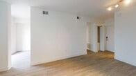 This well-appointed one-bedroom, one-and-a-half-bathroom residence offers a clean, modern aesthetic throughout its single-floor layout. Light wood-tone flooring flows consistently across all living areas, complementing the crisp white walls and creating a bright, cohesive atmosphere.

The living area is generously proportioned, featuring track lighting and large windows fitted with blinds that allow ample natural light to fill the space. An adjacent area provides additional flexible living space, also benefiting from the warm wood flooring and neutral palette.

The galley-style kitchen is efficiently designed with white shaker cabinetry, light countertops, a subway tile backsplash, and a stainless steel undermount sink with a brushed gold faucet. Stainless steel appliances, including a full-size refrigerator and dishwasher, complete the functional setup.

The bedroom is a comfortable size, featuring windows with outdoor views, a ceiling fan with light fixture, and the same wood-tone flooring found throughout.

The full bathroom includes a soaking tub with tiled surround, a white vanity with light countertops, and a large mirror. The half bathroom features a dual-sink vanity with white cabinetry and clean, minimal finishes, maintaining the unit's consistent modern character.