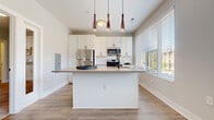 Located at 223 E Town St in the heart of downtown Columbus, Ohio, this one-bedroom, one-bathroom unit offers a thoughtfully designed single-floor layout with contemporary finishes. The kitchen serves as a central highlight, showcasing white shaker cabinetry, a classic subway tile backsplash, sleek countertops, and a full suite of stainless steel appliances including a range, over-the-range microwave, and refrigerator. A generously sized kitchen island with pendant lighting above provides both additional workspace and a natural gathering point. Large windows with horizontal blinds flood the kitchen and living areas with abundant natural light, offering views of the surrounding neighborhood. Wood-look flooring extends throughout the main living areas, lending warmth and cohesion to the open-concept space. The bedroom is a comfortable, carpeted retreat featuring soft, neutral walls and direct access to a dedicated walk-in closet equipped with wire shelving and hanging rods for well-organized storage. The bathroom is clean and functional, finished with wood-look tile flooring and a walk-in shower featuring tile surround and a sliding glass door. The overall aesthetic throughout the unit is modern and bright, with a neutral color palette that creates a welcoming and versatile living environment.