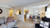 Located at 1 Marlbrook Ln in Lansdale, Pennsylvania, this single-floor residence offers a thoughtfully designed open-concept layout that seamlessly connects the main living areas. The living room features plush carpeting and a comfortable, well-appointed arrangement that invites relaxation. A half-wall pass-through connects the living space to the kitchen, enhancing the open feel while maintaining a sense of definition between rooms. The kitchen is equipped with stainless steel appliances, including a range and over-the-range microwave, and features warm wood-toned cabinetry paired with a clean, light countertop. The hard-surface flooring in the kitchen and dining area adds a sleek contrast to the carpeted living room. The dining area is positioned adjacent to the kitchen, accented by a pendant light fixture overhead and complemented by tasteful décor and artwork. Natural light flows throughout the space, contributing to a bright and airy ambiance. The overall design balances modern functionality with a warm, inviting aesthetic, making it a well-suited home for everyday living in the Lansdale community.