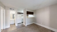 Located at 5915 Flintlock Rd in Houston, TX, this single-floor unit offers a practical and well-organized layout designed for comfortable everyday living. The interior is finished with neutral beige and warm gray tones throughout, creating a cohesive and calming atmosphere across all rooms.

The living room serves as the central gathering space, featuring plush carpeted flooring and a large window fitted with horizontal blinds that allows natural light to filter in while maintaining privacy. A built-in shelving unit adds functional storage and visual interest to the space. The kitchen area is positioned adjacent to the living room, separated by a half-wall counter, and is equipped with a range hood and refrigerator.

The bedroom is a generously sized private retreat, also finished with soft carpeting and neutral wall tones. A ceiling fan with integrated lighting provides both comfort and illumination, while a window with blinds allows natural light and outdoor views. A dedicated closet offers organized storage directly off the bedroom.

The unit also includes a bathroom, visible from the living area, finished with clean white fixtures. Hard wood-style flooring in the hallway and kitchen areas contrasts neatly with the carpeted living and sleeping spaces. Overall, the unit presents a clean, move-in-ready environment with a functional and straightforward design.