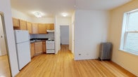 This single-floor unit is designed with functionality and warmth in mind, featuring light-toned hardwood floors that run consistently throughout the space, lending a sense of continuity and warmth to every room. The open living area is well-proportioned, with clean white walls, ceiling fans for added comfort, and classic cast-iron radiators that speak to the building's character and provide reliable heating.

The kitchen is efficiently laid out in an L-shaped configuration, equipped with light maple cabinetry offering generous storage, dark laminate countertops, a tile backsplash, a white gas range, and a full-size refrigerator. A double-basin sink anchors the corner layout, making the space both practical and easy to navigate.

The bedrooms are bright and well-sized, each featuring hardwood floors, ceiling fans, and large multi-pane windows that invite natural light and provide views of the surrounding brick exterior of neighboring buildings. The rooms offer a calm, neutral backdrop suited for a variety of uses.

The bathroom is finished in crisp white tile, featuring a full soaking tub with a shower, a single-basin vanity, and a small window above the tub that brings in natural light. Cast-iron radiators are present here as well, adding a touch of vintage charm. The overall layout is efficient and well-connected, making this a practical and inviting space.