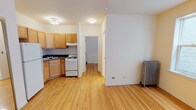This single-floor unit is designed with functionality and warmth in mind, featuring light-toned hardwood floors that run consistently throughout the space, lending a sense of continuity and warmth to every room. The open living area is well-proportioned, with clean white walls, ceiling fans for added comfort, and classic cast-iron radiators that speak to the building's character and provide reliable heating.

The kitchen is efficiently laid out in an L-shaped configuration, equipped with light maple cabinetry offering generous storage, dark laminate countertops, a tile backsplash, a white gas range, and a full-size refrigerator. A double-basin sink anchors the corner layout, making the space both practical and easy to navigate.

The bedrooms are bright and well-sized, each featuring hardwood floors, ceiling fans, and large multi-pane windows that invite natural light and provide views of the surrounding brick exterior of neighboring buildings. The rooms offer a calm, neutral backdrop suited for a variety of uses.

The bathroom is finished in crisp white tile, featuring a full soaking tub with a shower, a single-basin vanity, and a small window above the tub that brings in natural light. Cast-iron radiators are present here as well, adding a touch of vintage charm. The overall layout is efficient and well-connected, making this a practical and inviting space.