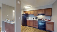Located at 5028 Dierker Rd in Columbus, Ohio, this single-floor residence offers a practical and comfortable layout with consistent finishes throughout. The kitchen is a functional highlight, featuring warm-toned wood cabinetry, granite-look countertops, a gas range with an overhead vent hood, a black refrigerator, and a double sink — all set atop durable wood-look flooring. A peninsula with a breakfast bar counter connects the kitchen to the adjacent living area, creating an open, accessible flow between spaces. The living room is generously sized, offering wood-look flooring, neutral taupe walls, a ceiling fan with light fixture, and a window that admits natural light. A hallway connects the main living areas to the private rooms, with wood-look flooring continuing underfoot and a textured ceiling overhead. The bedrooms are carpeted for comfort, with neutral gray walls and windows fitted with horizontal blinds that allow for natural light and privacy. The bathroom is well-equipped with a wooden vanity topped with granite-look countertops, a large framed mirror, and a tub-shower combination. Throughout the space, neutral tones, consistent flooring, and practical finishes create a clean, move-in ready environment suited for everyday living.