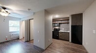 Located at 1435 W Talmage St in Springfield, MO, this one-bedroom, one-bathroom unit offers a thoughtfully designed layout that makes efficient use of its space. The interior features warm wood-look flooring throughout, neutral gray walls, and a textured ceiling that lend a cohesive, contemporary feel.

The kitchen is a standout feature, equipped with black appliances including an electric range, over-the-range microwave, and refrigerator. Rustic open wooden shelving mounted above a wood-grain tile backsplash provides both style and storage, while dark cabinetry and a clean white countertop complete the modern aesthetic.

The main living area is open and functional, anchored by the kitchen nook and flowing into the primary bedroom. The spacious bedroom accommodates a generous footprint and is fitted with a ceiling fan with light, providing comfort and circulation. A closet offers dedicated storage, keeping the living areas tidy and organized.

The bathroom is clean and straightforward, featuring a full-size soaking tub with a shower, white surround walls, and wood-look accents that tie into the overall design theme. A window in the living area allows natural light to filter into the space. This unit offers a practical, move-in-ready option with updated modern finishes throughout.