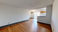 This efficiently laid-out one-bedroom, one-bathroom unit is organized across a single floor, making the most of its compact footprint. The open-concept living and dining area flows seamlessly into the kitchen, creating a connected and functional living space. Hardwood-style flooring runs throughout the main living areas, adding warmth and continuity to the design. A textured ceiling adds architectural character to the space.

The kitchen features warm wood cabinetry, a dark granite-style countertop, a white electric range, a refrigerator, and a sink — all oriented around a peninsula that separates the kitchen from the living area. A sliding glass door off the living room opens onto a private balcony with outdoor views of surrounding greenery, allowing natural light to fill the space.

The bedroom is a comfortable, well-proportioned room finished with plush carpet and a ceiling fan with lighting. A window with blinds frames a pleasant view of trees, and a baseboard heater ensures year-round comfort. The room also includes a closet for storage.

The bathroom is clean and well-appointed, featuring a tub-shower combination, a white vanity with granite-style countertop, a mirrored medicine cabinet, and tile flooring. A hallway connects the main living areas to the bedroom and bathroom, completing this practical and livable layout.