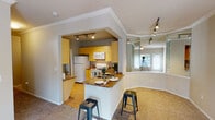 This single-floor residence is designed with a practical, open layout that connects its living and kitchen areas seamlessly. The kitchen is well-appointed with warm yellow cabinetry, granite-style countertops, white appliances including a refrigerator, electric range, and over-the-range microwave, and hardwood-style flooring. A peninsula with a built-in sink and dark granite countertop extends into the living area, accompanied by metal bar stools that create a casual dining space. Track lighting overhead illuminates both the kitchen and adjacent areas effectively. Crown molding runs throughout, adding a polished architectural detail to the space.

A distinctive curved bay window nook sits adjacent to the kitchen, framed by floor-to-ceiling mirrored panels that amplify natural light and create a sense of added depth. Carpeted throughout the living and bedroom areas, the space maintains a cohesive, comfortable feel. The bedrooms are generously proportioned, each featuring ceiling fans, neutral carpet, and windows with blinds that allow for natural light while maintaining privacy.

The unit includes two bathrooms, both finished with matching granite countertops and light wood cabinetry. One bathroom features a single-sink vanity with overhead storage, while the larger bathroom offers a wide granite-topped vanity with a broad mirror and well-lit fixture above. Both bathrooms include a tub-shower combination with white tile surround and tile flooring.