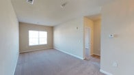 This single-story residence offers two bedrooms and two bathrooms within a clean, functional layout. The interior is finished with wall-to-wall neutral-toned carpeting that runs throughout the main living areas, complemented by smooth beige walls and crisp white baseboards that create a bright, cohesive aesthetic. A generously sized window in the main room allows natural light to fill the space, enhancing the open, airy feel of the interior. The ceiling is standard height with a centrally located smoke detector, and multiple electrical outlets are positioned conveniently along the walls. A doorway visible from the main living area leads to an adjacent room, suggesting a straightforward and accessible floor plan that connects living and private spaces with ease. The overall design is understated and move-in ready, providing a neutral canvas suitable for a variety of furnishing styles. The combination of light walls, soft carpeting, and natural light contributes to a calm and welcoming atmosphere throughout the unit.