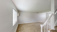 Located at 739 Patterson Rd in Dayton, Ohio, this two-story home offers a practical and functional layout across two floors. The main level houses the kitchen, which features white cabinetry, laminate countertops, a single-basin sink, tile flooring, and white appliances including a range and refrigerator. Open shelving adds additional storage, while a textured ceiling adds character to the space. A staircase connects the two floors, finished with white balusters and warm wood treads. The upper level features two carpeted bedrooms and a shared bathroom. The primary bedroom offers a comfortable footprint with natural light filtering in through windows fitted with blinds. The second bedroom similarly features neutral carpet, soft grey walls, and windows overlooking the surrounding greenery. Both bedrooms feature panel-style doors and clean white trim throughout. The shared bathroom includes a tub-shower combination with wall surround and a window for natural ventilation. Consistent textured ceilings, neutral grey walls, and tan carpeting throughout the upper floor create a cohesive and understated aesthetic. A hallway connects the upper-level rooms, contributing to a straightforward and efficient floor plan.