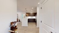 This thoughtfully designed one-bedroom, one-bathroom residence at 15 High St. in Norwell, MA, offers a well-appointed single-floor layout that maximizes both function and style. The open-concept living area anchors the home, featuring light hardwood flooring, recessed lighting, and a set of French doors that invite natural light and provide access to the outdoors. The living room flows seamlessly into the dining area, which is brightened by multiple windows fitted with clean white blinds and accented by a striking multi-arm Edison-bulb chandelier. The kitchen is a standout, equipped with rich dark-walnut cabinetry extending to the ceiling, crisp white countertops, a central island with seating, stainless steel appliances, and elegant pendant lighting. The bedroom is a serene retreat with light-toned walls, hardwood-style flooring, and a generously sized window that fills the room with natural light. The bathroom features a clean, modern aesthetic with marble-look tile flooring, subway tile surrounding the tub and shower, a dark-wood vanity with a white countertop, and a bright, airy finish throughout. A connecting hallway completes the efficient and cohesive floor plan of this well-crafted Norwell residence.