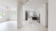 Located at 8000 West Dr in North Bay Village, Florida, this single-floor residence showcases a clean, modern design with a bright, open layout. Large format white tile flooring flows consistently throughout the space, enhancing the sense of openness and reflecting abundant natural light.

The contemporary kitchen serves as the centerpiece of the living area, equipped with stainless steel appliances including a French door refrigerator, electric range, and microwave. Two-tone cabinetry pairs dark lower cabinets with light gray upper cabinets, complemented by a subway tile backsplash and granite countertops. A kitchen island with a matching granite surface provides additional workspace and casual seating. Pendant lights and track lighting complete the kitchen's polished look.

The open living and dining area is defined by structural columns and large windows that invite views of tropical palm trees, creating a connection to the lush South Florida surroundings. The bedrooms are well-proportioned, each featuring tile flooring, ceiling fans or overhead lighting, and windows with blinds framing tropical scenery.

The bathrooms are finished with large-format gray wall tile, granite vanity countertops, and dark wood-toned cabinetry. One bathroom features a separate soaking tub and walk-in shower, while the second offers a tub-shower combination. A louvered utility closet provides convenient in-unit storage. The overall aesthetic is consistently modern, light, and airy throughout.