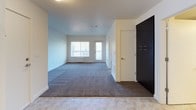 This single-floor unit presents a clean, contemporary design throughout its well-organized layout. The kitchen is a standout feature, outfitted with dark navy cabinetry, granite-look countertops, and a full suite of stainless steel appliances including a refrigerator, electric range, built-in microwave, and dishwasher. A textured tile backsplash adds visual interest, while light-toned flooring ties the space together. Recessed fluorescent lighting illuminates the kitchen efficiently.

The open living area transitions seamlessly from the kitchen entry, featuring plush grey patterned carpeting and neutral white walls that create a bright, versatile canvas. A large closet with dark panel doors provides ample storage near the entry. The living space extends toward a glass door and window that open to a private balcony, allowing natural light to flow in and offering views of surrounding greenery.

The bedroom is a calm, well-proportioned space with the same grey carpeting, white walls, and a wide window fitted with horizontal blinds that frame outdoor tree views.

The bathroom features a full-size soaking tub with an overhead shower, a curved curtain rod, brushed nickel fixtures, tile flooring, and a granite-topped vanity — delivering a functional and polished finish.