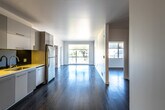 This single-floor unit presents a clean, contemporary design defined by crisp white walls, smooth ceilings, and rich dark hardwood flooring that runs consistently throughout the space. The open-plan layout connects the kitchen directly to the living area, creating a generous, flowing communal zone. Large windows at the far end of the living space admit abundant natural light and offer outdoor views, enhancing the sense of openness.

The kitchen is well-equipped with flat-front grey cabinetry extending to the ceiling for ample storage, a dark reflective backsplash, light countertops, a gas cooktop, built-in oven, stainless steel refrigerator, and an undermount sink. The contrast between the cabinetry and backsplash gives the kitchen a sleek, modern character.

The bedrooms are generously proportioned, featuring white walls, dark hardwood floors, and sliding-door closets with built-in hanging rods providing practical storage. The bathrooms are finished in a clean, minimalist style with white subway tile surrounding the bathtub and shower, a floating white vanity with an integrated sink, a large mirror, and dark mosaic tile flooring, completing the unit's cohesive modern aesthetic.