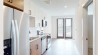 Located at 1290 Old Peachtree Rd NW in Duluth, GA, this modern single-floor residence offers a clean, contemporary design throughout. The open-concept layout connects the kitchen and living areas seamlessly, creating a bright and airy atmosphere enhanced by recessed lighting and warm hardwood-style flooring that runs throughout the space.

The kitchen is well-appointed with stainless steel appliances including a refrigerator with ice maker, electric range, built-in microwave, and dishwasher. A dual-tone cabinetry scheme pairs white upper cabinets with warm wood-toned lower cabinets, complemented by granite countertops, a white subway tile backsplash, and a black matte faucet over a stainless steel sink.

The living area is generously sized with a ceiling fan, large windows, and a glass door that opens directly onto a private balcony, allowing abundant natural light and outdoor views to fill the room.

The bathroom features a warm wood vanity with granite countertop, a large mirror, contemporary light fixtures, and a glass-enclosed walk-in shower.

A wide entry hallway connects all areas of the home, finished with the same consistent flooring and neutral white walls, giving the entire space a cohesive, modern aesthetic.
