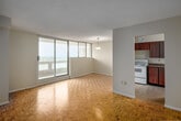 This 2-bedroom, 1-bathroom unit at 210 Steeles Ave W in Brampton, Ontario offers a well-organized layout across a single floor. The interior is unified by warm parquet flooring throughout, lending a classic character to each room. The open living and dining area is bright and airy, highlighted by large floor-to-ceiling sliding glass doors that lead to a private balcony offering sweeping elevated views of the surrounding Brampton landscape. A pendant light fixture anchors the dining space, which flows seamlessly toward the kitchen. The kitchen is separate and efficiently designed, featuring rich wood cabinetry, a double sink, laminate countertops, white appliances including a stove and refrigerator, and tile flooring. Both bedrooms are comfortably sized, each featuring sliding wood-panel closet doors and parquet flooring. The primary bedroom benefits from wide windows that fill the room with natural light and provide additional outdoor views. The bathroom is clean and functional, complete with a full tiled tub-shower surround, vanity with sink, and white tile flooring. A hallway connects all rooms, contributing to the unit's practical and efficient flow throughout.