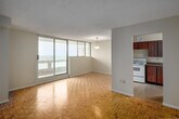 This 2-bedroom, 1-bathroom unit at 210 Steeles Ave W in Brampton, Ontario offers a well-organized layout across a single floor. The interior is unified by warm parquet flooring throughout, lending a classic character to each room. The open living and dining area is bright and airy, highlighted by large floor-to-ceiling sliding glass doors that lead to a private balcony offering sweeping elevated views of the surrounding Brampton landscape. A pendant light fixture anchors the dining space, which flows seamlessly toward the kitchen. The kitchen is separate and efficiently designed, featuring rich wood cabinetry, a double sink, laminate countertops, white appliances including a stove and refrigerator, and tile flooring. Both bedrooms are comfortably sized, each featuring sliding wood-panel closet doors and parquet flooring. The primary bedroom benefits from wide windows that fill the room with natural light and provide additional outdoor views. The bathroom is clean and functional, complete with a full tiled tub-shower surround, vanity with sink, and white tile flooring. A hallway connects all rooms, contributing to the unit's practical and efficient flow throughout.
