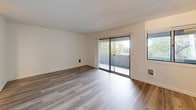 This well-appointed single-floor unit offers a clean, modern aesthetic defined by crisp white walls, light wood-style flooring, and an abundance of natural light throughout. The open living area is a welcoming focal point, featuring sliding glass doors that lead to a private balcony overlooking lush greenery — flooding the space with natural light and providing a seamless indoor-outdoor connection. A secondary window further enhances the airy feel of the living space.

The kitchen is efficiently designed with a galley-style layout, showcasing white cabinetry with modern hardware, dark quartz countertops, a contemporary sink with a gooseneck faucet, and black appliances including an electric range and refrigerator. Track lighting overhead ensures the workspace is well-lit.

The bedrooms are thoughtfully designed with ceiling fans fitted with integrated lighting, neutral walls, and windows that frame views of the surrounding greenery. The light-toned flooring and roller shades contribute to a calm, restful atmosphere.

The bathroom features a clean, all-white design with a full tub-shower combination, a wood-toned vanity, and light wood-style flooring that ties the space cohesively to the rest of the unit. The overall ambiance is fresh, modern, and move-in ready.
