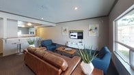 Located at 301 T St in Tumwater, Washington, this community lounge offers a well-appointed gathering space designed for comfort and relaxation. The single-floor layout features a thoughtfully arranged seating area anchored by a rich brown leather sofa and complementary blue accent chairs, all positioned around a wooden coffee table. A wall-mounted flat-screen TV with a white media console serves as the focal point on one wall, flanked by colorful abstract artwork that adds a modern touch to the neutral color palette.

The space is finished with plush dark carpeting underfoot and a textured ceiling with recessed lighting that creates a warm, inviting ambiance. Crown molding along the upper walls adds a refined architectural detail. Natural light filters in through large windows that offer views of mature trees outside, brightening the lounge during the day.

Decorative greenery, including potted aloe and other plants, is placed throughout the space, contributing to a fresh and lively atmosphere. A bar-height counter with stools provides an additional casual seating option. French doors with glass panels connect the lounge directly to an adjacent fitness center, which is visible through mirrored walls, making this lounge a central hub for both relaxation and an active lifestyle.