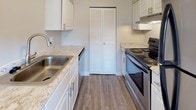 Located at 841 Gawain Cir in Dayton, Ohio, this single-floor home offers a practical and well-organized layout designed for comfortable everyday living. The galley-style kitchen is outfitted with white cabinetry, light stone-pattern laminate countertops, a stainless steel sink, and a stainless electric range, complemented by wood-look vinyl plank flooring that adds warmth and durability. A louvered bifold door provides access to a pantry or utility closet, offering convenient built-in storage. The kitchen opens toward the dining and living areas, where a pendant light fixture anchors the transition between spaces. The living areas feature neutral-toned carpet and large windows that allow natural light to fill the rooms, creating a bright and airy atmosphere. The spacious main living room benefits from an additional window with outdoor views, enhancing the sense of openness. The bedrooms are generously sized, each with soft carpeting, neutral wall tones, and ample room for furnishings. The full bathroom is cleanly appointed with a white vanity, light countertop, an illuminated mirror cabinet, and a tub-shower combination, all set on wood-look flooring. The home's cohesive neutral palette and functional design make it a versatile and move-in ready space.