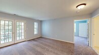 Located at 1 Jenny Lind St in Netcong, NJ, this well-appointed one-bedroom, one-bathroom residence offers a thoughtfully organized single-floor layout. The combined kitchen and living area serves as the heart of the home, with the kitchen featuring warm honey-toned oak cabinetry, a gray stone tile backsplash, light wood laminate flooring, and white appliances including a coil-top range, over-the-range microwave, and dishwasher. The living room area is generously sized, finished with plush carpeting in a neutral tone, and bathed in natural light through French doors that open to an outdoor view, complemented by an additional side window. The spacious primary bedroom is dressed in soft blue-gray paint, plush carpet, and multiple windows framing lush greenery outside. It connects directly to a dedicated walk-in closet equipped with wire shelving for practical storage. The full bathroom is clean and functional, offering a tub/shower combination with safety grab bars, a single-sink vanity with a large mirror, and classic mosaic tile flooring. Throughout the residence, a consistent palette of light blue-gray walls and white trim creates a calm, cohesive ambiance.