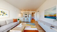 Located at 875 NE 27th Ave in Portland, Oregon, this well-designed one-bedroom, one-bathroom residence offers a thoughtfully arranged single-floor layout. Light wood flooring flows throughout the main living areas, creating a warm and cohesive aesthetic.

The open-concept kitchen and living room serve as the heart of the home. The kitchen features sleek flat-front cabinetry, stainless steel appliances including a refrigerator, range, microwave, and dishwasher, a white subway tile backsplash, and a peninsula countertop with bar seating beneath stylish pendant lighting. The living area is bright and airy, anchored by large windows and a glass sliding door that bring in generous natural light and offer views of the surrounding neighborhood.

The hallway connects to a dedicated closet and leads to the private bedroom, which offers a comfortable footprint, plush carpeting, a window with outdoor views, and a louvered closet door for storage. The full bathroom is clean and modern, with light tile flooring, a wide vanity with under-mount sink and quartz-style countertop, a large mirror, and a shower-tub combination. Throughout the residence, the design maintains a bright, contemporary feel with neutral tones and modern finishes.