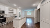 Located at 14350 Ambrosia Street in Tampa, FL, this well-appointed 2-bedroom, 2-bathroom single-story home offers a thoughtfully designed open-concept layout. The kitchen serves as the centerpiece of the main living area, featuring a granite-topped island with warm wood-toned cabinetry, white upper cabinets, a subway tile backsplash, stainless steel appliances, and recessed lighting. The kitchen flows seamlessly into the spacious living room, which is filled with natural light from a large window and finished with a ceiling fan overhead. Rich wood-look flooring runs throughout the entire home, adding warmth and continuity to each space. The primary bedroom is generously sized, offering a ceiling fan, a bright window with outdoor views, and access to a walk-in closet with wire shelving. The bathrooms are finished with granite vanity tops and wood-toned cabinetry, consistent with the home's modern aesthetic. A second well-proportioned bedroom and a connecting hallway complete the layout. Two closets provide ample storage throughout. Clean white walls, modern door hardware, and recessed lighting contribute to a bright, contemporary ambiance throughout this move-in-ready Tampa home.