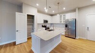 This single-floor residence in Morrisville, NC offers a thoughtfully designed layout with modern finishes throughout. The kitchen serves as a standout centerpiece, featuring crisp white shaker-style cabinetry extending to the ceiling, quartz countertops, stainless steel appliances including a French door refrigerator and electric range, and a large center island with a deep double-basin sink. Pendant globe lighting and recessed fixtures illuminate the space, while light hardwood flooring adds warmth. A dedicated walk-in pantry provides generous storage. The bedrooms are carpeted in neutral tones and bathed in natural light through blinds-fitted windows. Ceiling fans with integrated lighting are featured in select rooms for added comfort. The bathrooms are finished with marble-style tile surround, offering both a soaking tub with brushed gold fixtures and a separate glass-enclosed walk-in shower with matching gold hardware. Bedrooms also include access to walk-in closets, adding practical storage. The open floor plan, visible in the 3D overview, connects the main living areas seamlessly, creating a cohesive and functional living environment suited for modern lifestyles.