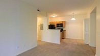 Located at 471 N Hamilton Rd in Gahanna, Ohio, this single-floor unit offers a practical and open layout designed for comfortable everyday living. The living area features neutral-toned carpeting that extends throughout the space, creating a cohesive and understated aesthetic.

The kitchen is positioned adjacent to the living area and is partially separated by a half-wall peninsula, which provides both a visual boundary and additional counter space. Warm honey-toned wood cabinetry lines the kitchen walls, complemented by dark granite-style countertops and black appliances, including a refrigerator, microwave, and range. A pendant light hangs above the peninsula, adding a focused point of illumination to the kitchen area.

The living space is bright and open, with light-colored walls that reflect the overhead lighting effectively. A hallway visible from the main living area provides access to additional rooms within the unit. An electrical panel is conveniently accessible along the hallway wall. The overall ambiance is clean and functional, with a neutral palette that offers flexibility for a variety of interior styles.
